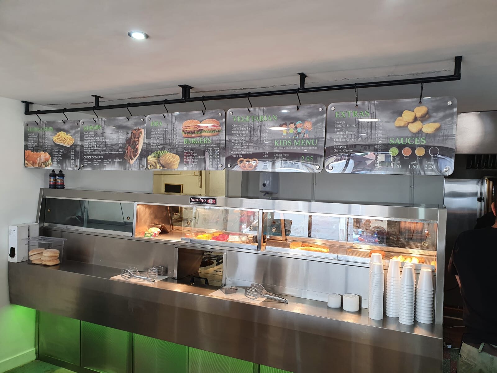 Printed menu panels hung from a black rail above a fish and chip counter
